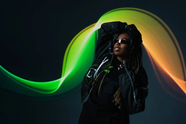 Stylish african american woman in smart glasses standing on grey background with abstraction — Stock Photo