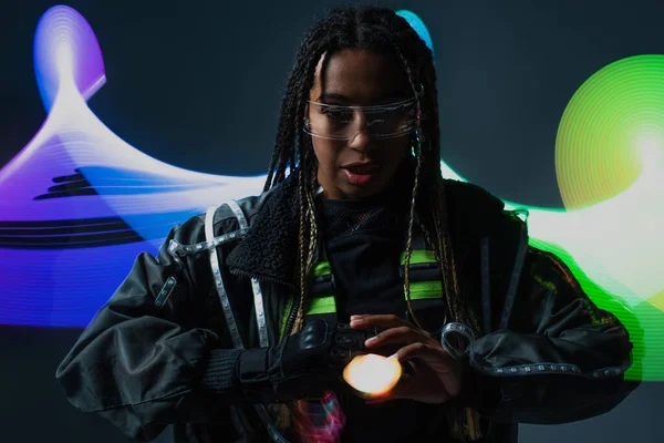 Elegante mujer afroamericana en gafas inteligentes de pie cerca de la abstracción sobre fondo gris - foto de stock