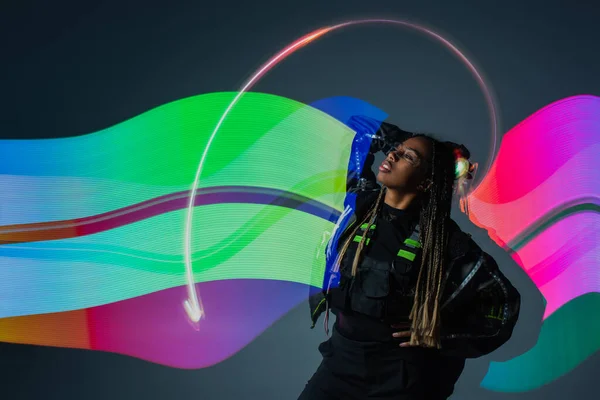 Esposa larga de mujer afroamericana en gafas inteligentes posando cerca de la abstracción sobre fondo gris - foto de stock