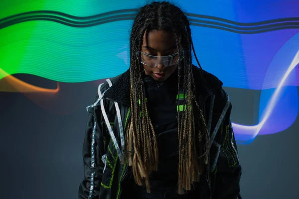 Mujer afroamericana en gafas inteligentes de pie cerca de la abstracción sobre fondo gris - foto de stock