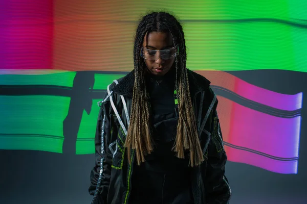 Stylish african american woman in smart glasses standing near colorful abstraction on grey background — Stock Photo