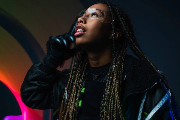 Stylish african american woman in cyber glove and smart glasses standing on grey background with abstraction — Stock Photo