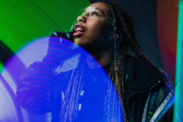 African american woman in smart glasses and cyber glove looking away near abstracted lights on grey background — Stock Photo