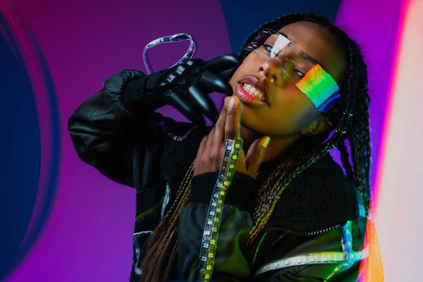 Elegante mujer afroamericana en gafas inteligentes mirando a la cámara en un fondo colorido - foto de stock