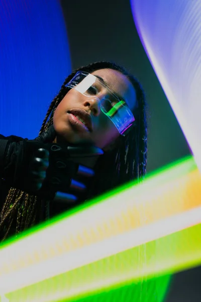 African american woman in cyber glove and smart glasses looking at camera on colorful background — Stock Photo