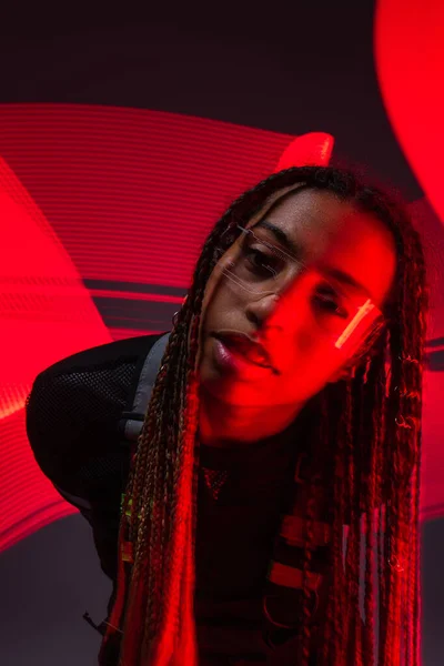 Femme afro-américaine élégante en lunettes intelligentes regardant la caméra sur fond gris avec des lumières rouges — Photo de stock