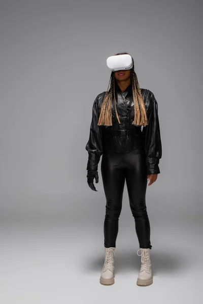 Mujer afroamericana en guante cibernético y auriculares vr sobre fondo gris - foto de stock