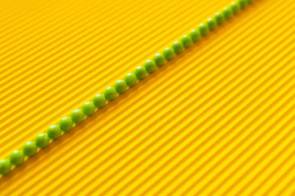 Vista superior de la línea diagonal de pequeñas bolas verdes sobre fondo corrugado amarillo - foto de stock