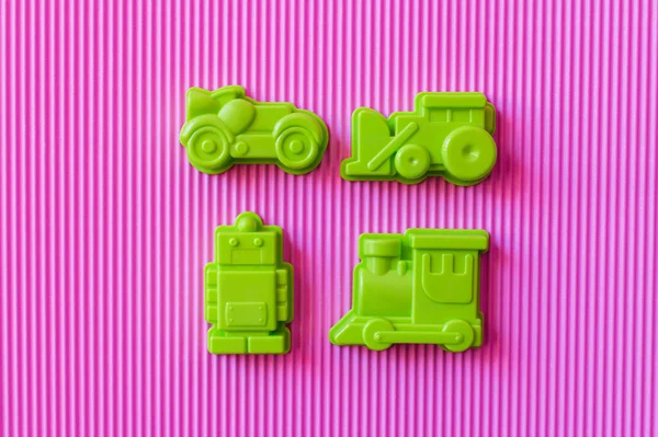 Top view of green toy robot near plastic vehicles on violet textured background — Stock Photo