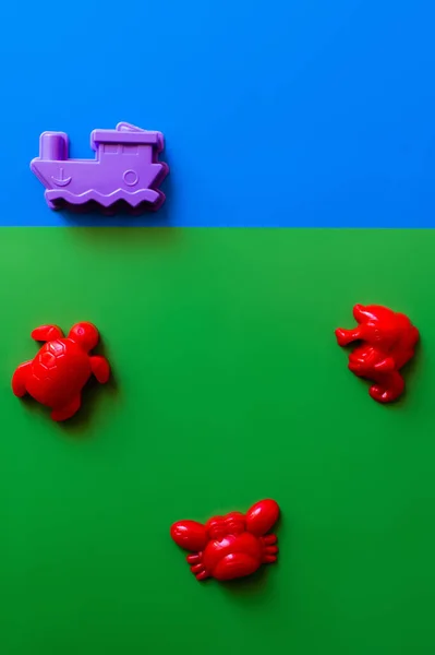 Vista superior de animales de mar rojos y juguetes de barco púrpura sobre fondo azul y verde - foto de stock