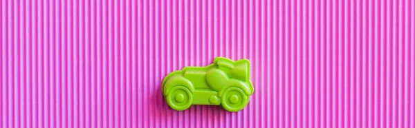 Вид зверху на зелений старовинний іграшковий автомобіль на фіолетовому гофрованому фоні, банер — стокове фото