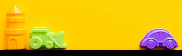 Top view of multicolored plastic vehicles and tower on black and yellow background, banner — Stock Photo