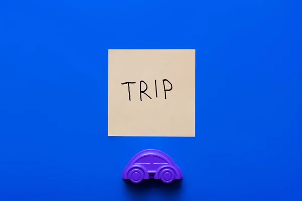 Верхний вид бумажной карточки с буквами поездки рядом с фиолетовым игрушечным автомобилем на синем фоне — стоковое фото