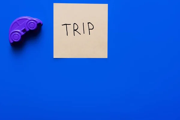 Top view of purple plastic car near card with trip lettering on blue background — Stock Photo