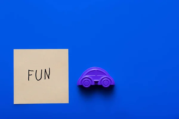 Vue du dessus du papier avec lettrage amusant près de la moisissure de voiture violette sur fond bleu — Photo de stock