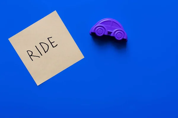 Draufsicht auf Papier mit Aufschrift in der Nähe von lila Spielzeugauto auf blauem Hintergrund — Stockfoto