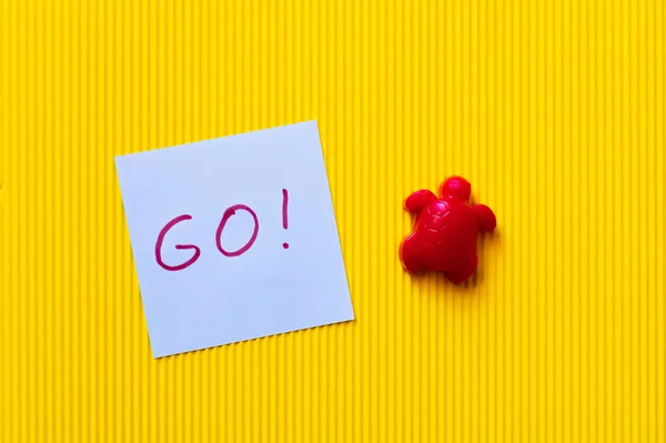 Vista superior de tartaruga de plástico vermelho perto de papel azul com letras go no fundo amarelo — Stock Photo