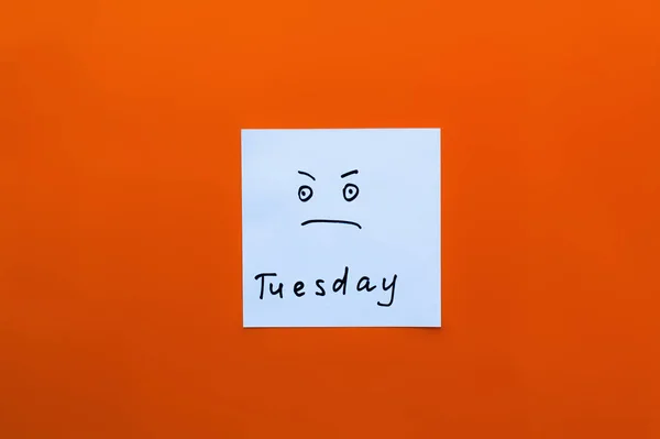 Top view of card with displeased emoji and tuesday lettering on orange background — Stock Photo