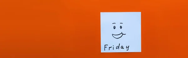 Top view of cheerful emoticon near friday lettering on sticky note on red background, banner — Stock Photo