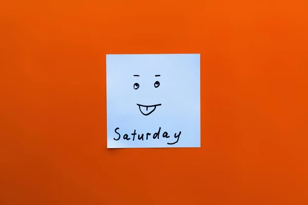 Top view of sticky note with saturday inscription and sticking out tongue emoji on red background — Stock Photo