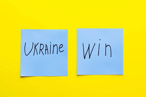 Top view of blue papers with ukraine win lettering on yellow background — Stock Photo