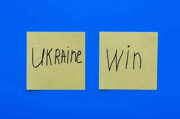 Vue du dessus des cartes en papier avec lettrage ukraine win sur fond bleu — Photo de stock