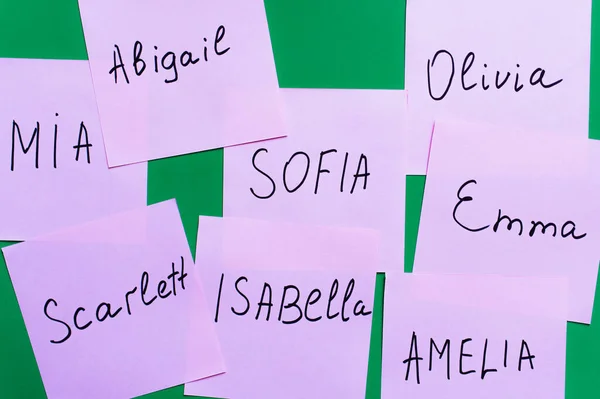 Top view of pale purple cards with female names on green background — Stock Photo