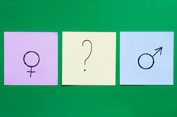 Vista superior de cartões multicoloridos com ponto de interrogação entre os sinais de gênero no fundo verde — Fotografia de Stock