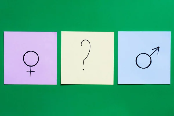 Top view of multicolored cards with question mark between gender signs on green background — Stock Photo