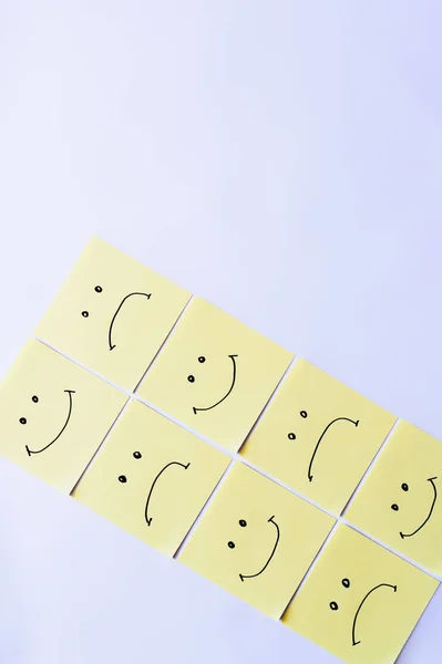 Top view of pale yellow sticky notes with happy and upset emoji on white background — Stock Photo