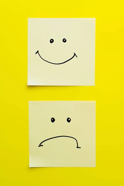 Top view of sticky notes with joyful and sad smileys on bright yellow background — Stock Photo