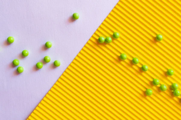 Top view of small green balls on violet and yellow textured background — Stock Photo