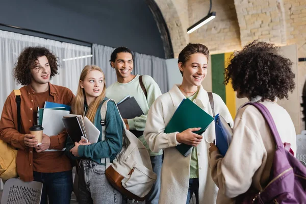 Sorrindo estudantes multiétnicos com mochilas e cadernos conversando na universidade — Fotografia de Stock