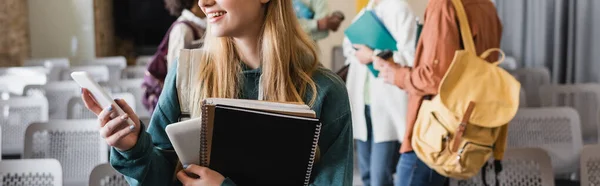 Visão parcial da mulher com livros de cópia e smartphone perto de estudantes inter-raciais em fundo turvo, banner — Fotografia de Stock