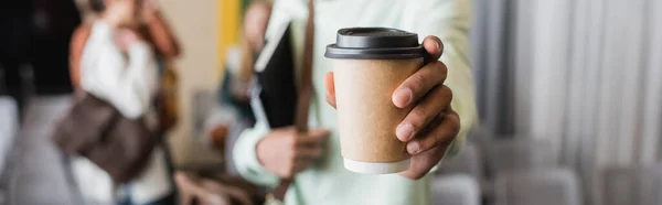 Cropped view of african american student holding coffee to go on blurred background, banner — Stock Photo