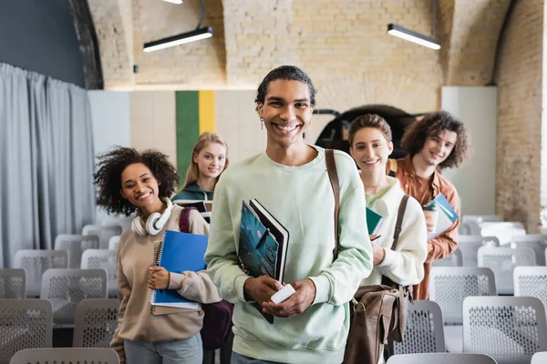 Happy african american man looking at camera together with multiethnic friends in auditorium — Stock Photo