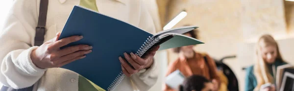Cropped view of woman with notebooks near multiethnic students on blurred background, banner — Stock Photo