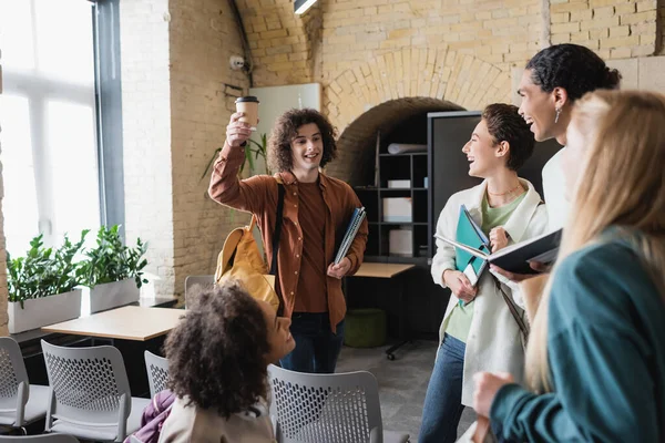 Happy man toasting with paper cup near smiling multiethnic classmates in university — Stock Photo