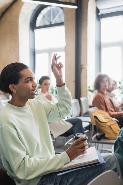 Африканский американский студент с кофе пойти и поднял руку задавая вопрос во время лекции в университете — стоковое фото