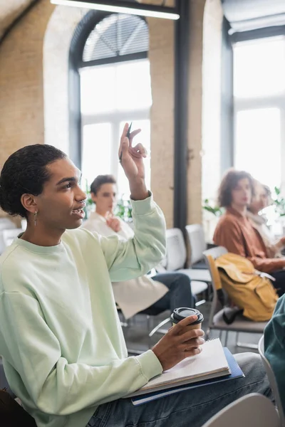 Étudiant afro-américain avec café pour aller et a levé la main poser la question pendant la conférence à l'université — Photo de stock