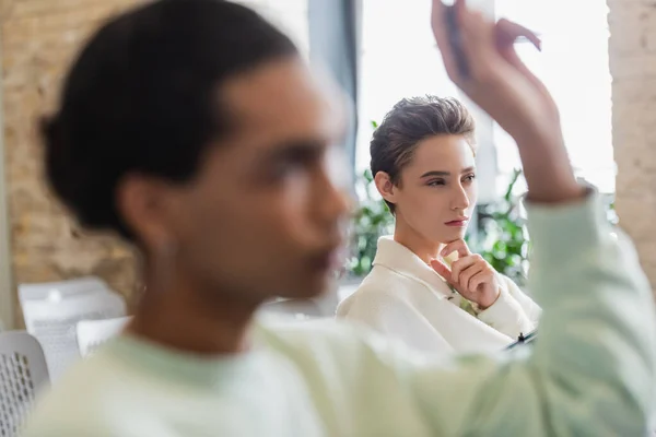 Pensativa mujer escuchando conferencia cerca borrosa afroamericano hombre con la mano levantada - foto de stock