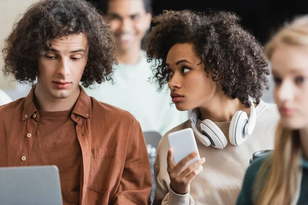 African american woman with mobile phone and headphones talking to curly friend in classroom — Stock Photo