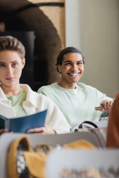 Giovane uomo africano americano sorridente durante la lezione in università vicino compagno di classe offuscata — Foto stock