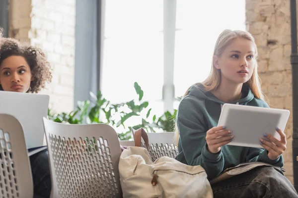 Fokussierte Frau hält digitales Tablet während des Unterrichts in der Nähe einer verschwommenen afrikanisch-amerikanischen Klassenkameradin — Stockfoto