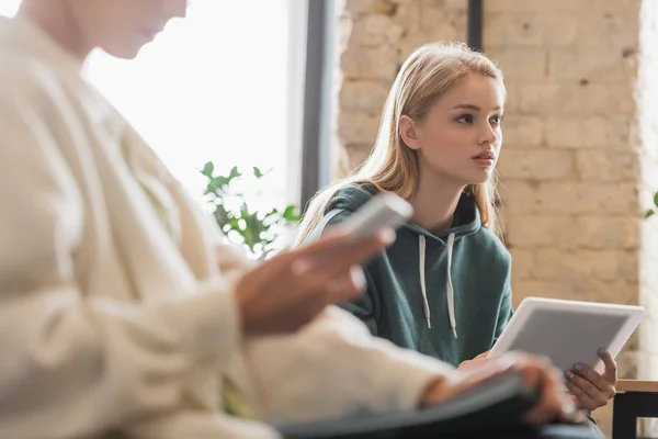 Konzentrierte Studentin hält digitales Tablet in der Nähe verschwommener Freundin während Vorlesung — Stockfoto