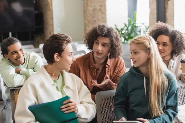 Estudiante rizado señalando con la mano mientras habla cerca de amigos multiétnicos en el aula — Stock Photo