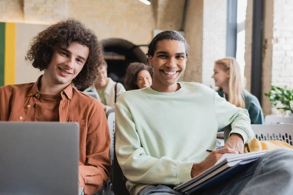 Estudante americano africano feliz e seu amigo com laptop olhando para a câmera durante a palestra — Fotografia de Stock