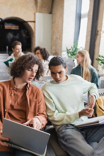 Lockige Studentin zeigt im Hörsaal auf Laptop neben afrikanisch-amerikanischem Freund — Stockfoto