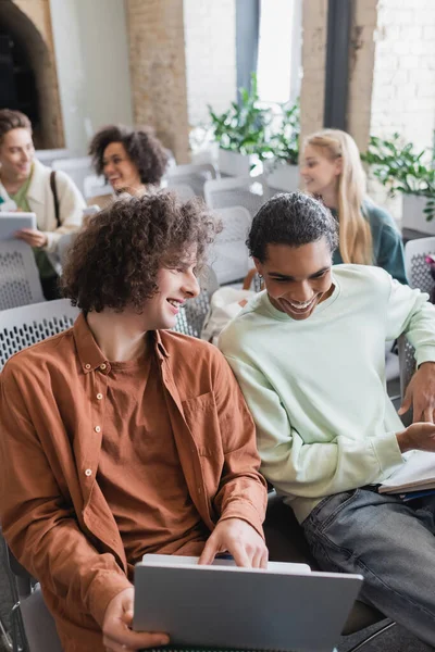 Afrikanisch-amerikanischer Student lächelt neben Freund, der mit Laptop im Hörsaal sitzt — Stockfoto