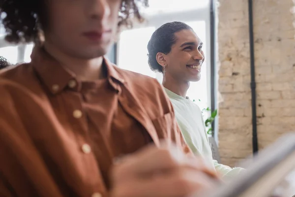 Young african american student smiling near blurred friend during lecture in university — Stock Photo